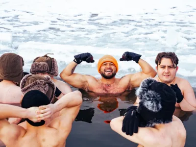 A man in an orange Central Waste beanie is flexing in an ice bath surrounded by other men